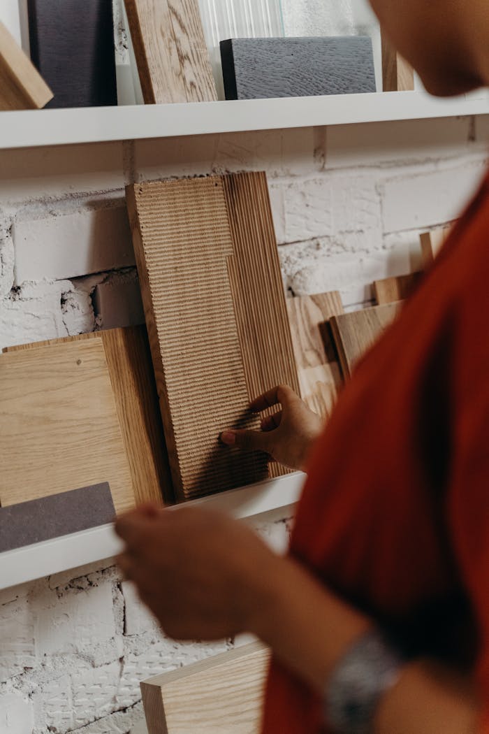 gallery-4 Close-up of a person selecting wooden material samples from a display shelf against a brick wall.