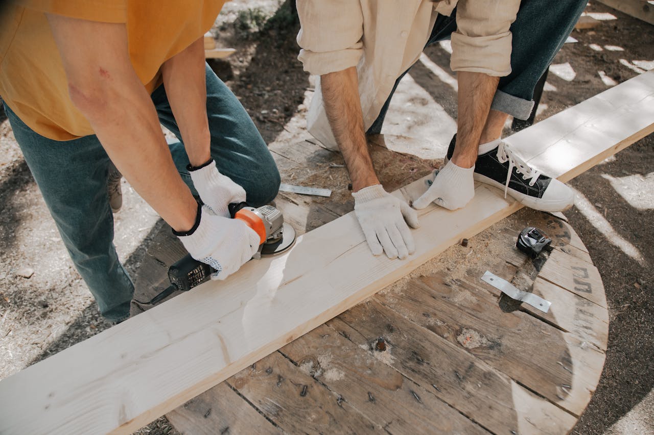 Two young carpenters using electric tools on a wooden plank outdoors. Practical DIY woodworking scene.