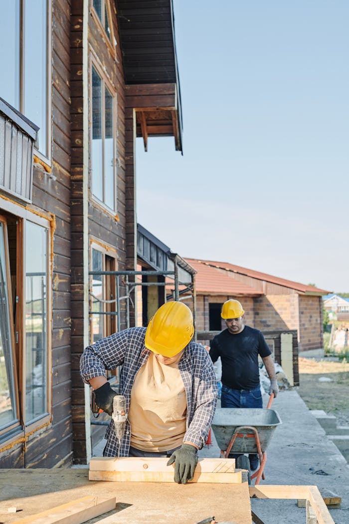 services-04 Two workers in hard hats engaged in carpentry at a construction site, building a wooden house.